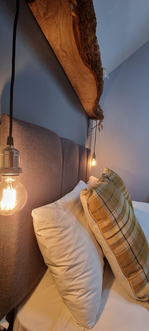 A bed with a headboard, a hanging light fixture, and a wall-mounted shelf with a plant.