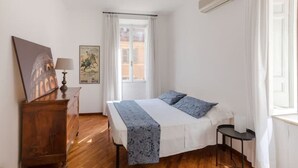 Un dormitorio con cama, mesita de noche, lámpara, cartel y ventana con cortinas.