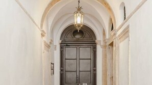 Un pasillo con una puerta de madera oscura, paredes blancas y suelo de baldosas.