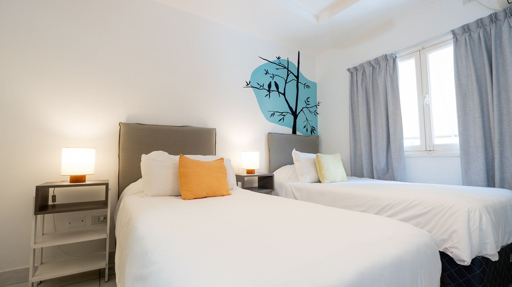 Une chambre d’hôtel avec deux lits, deux tables de chevet, une décoration murale en forme d’arbre et une fenêtre avec des rideaux.