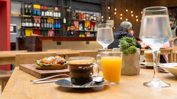 Un comedor con una mesa de madera dispuesta con un sándwich, una taza de café, un vaso de jugo de naranja y una copa de martini.