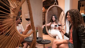 Un grupo de personas sentadas en una silla de mimbre, sosteniendo copas de vino, con una botella sobre una mesita.