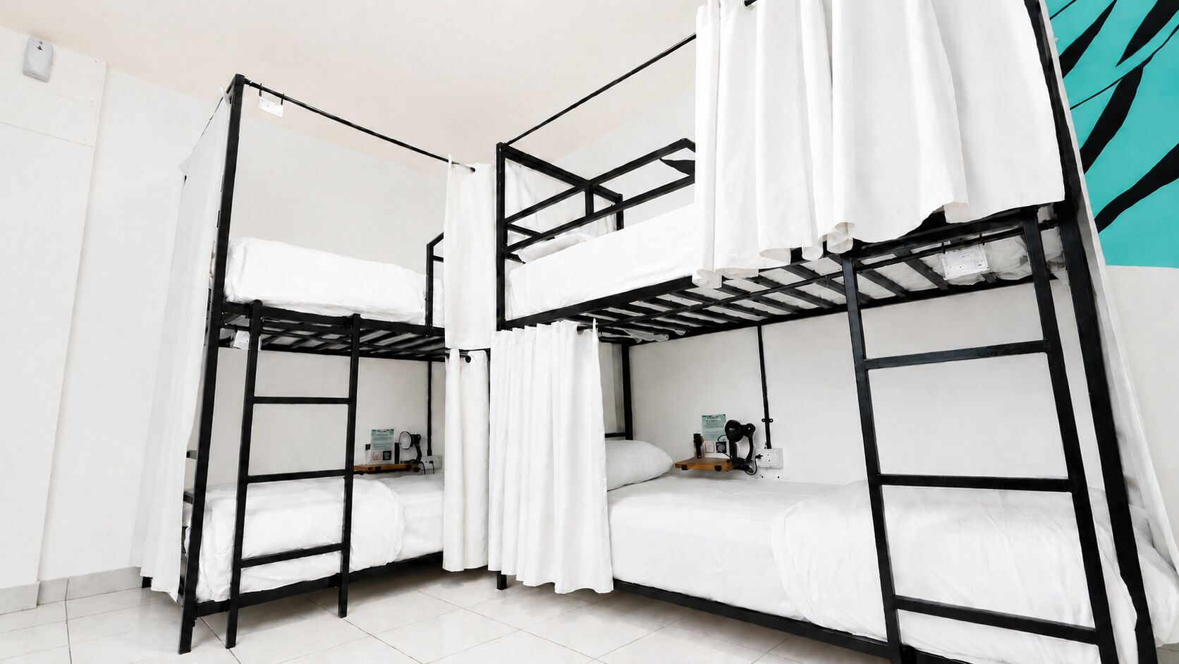 Une chambre avec un lit superposé, du linge de lit et des rideaux blancs, une petite table avec une chaise et une prise électrique fixée au mur.
