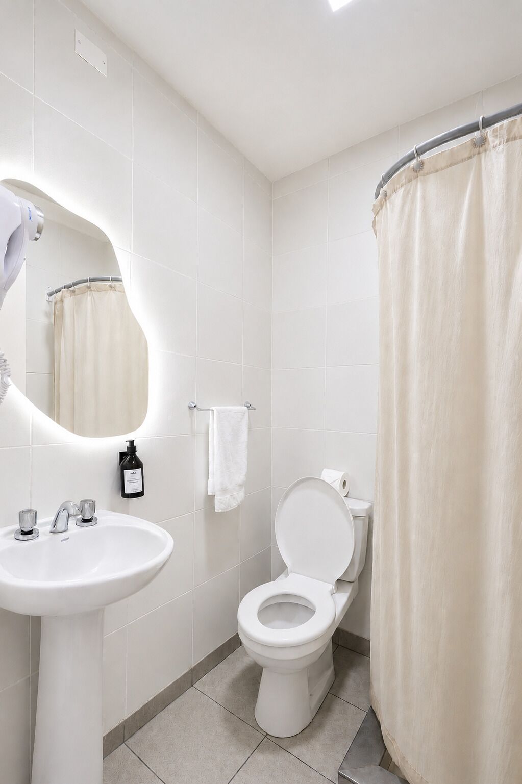 Une salle de bain avec un lavabo blanc, des toilettes, un rideau de douche et un miroir.