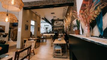 Interior de una cafetería con mesas y sillas de madera, una barra y un tablero de menú visible.