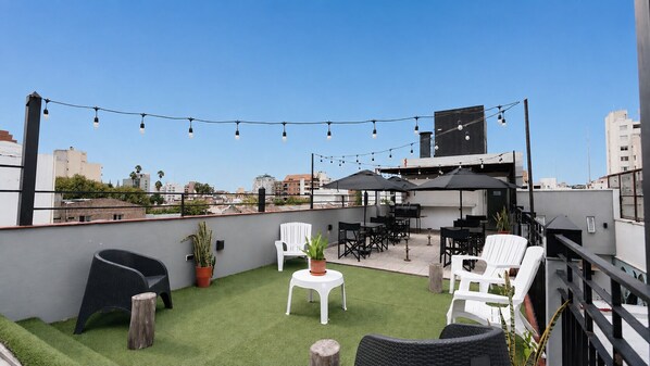 Terraza en la azotea con césped artificial, mobiliario exterior, luces colgantes y vistas de la ciudad.