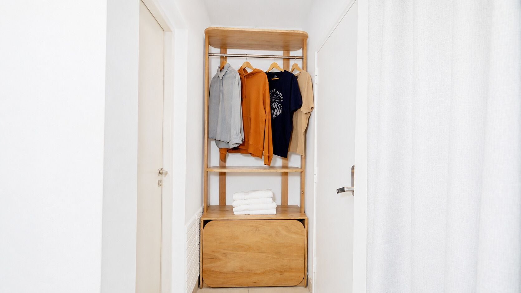 Un vestidor con estantes de madera, una barra para colgar ropa y un banco con toallas dobladas.