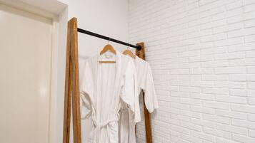 Pared de ladrillo blanco con un perchero de madera que sostiene batas blancas.