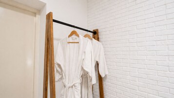 Pared de ladrillo blanco con un perchero de madera que sostiene batas blancas.