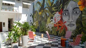 Un área de estar al aire libre con suelo a cuadros, macetas con plantas y un mural de flores y follaje.