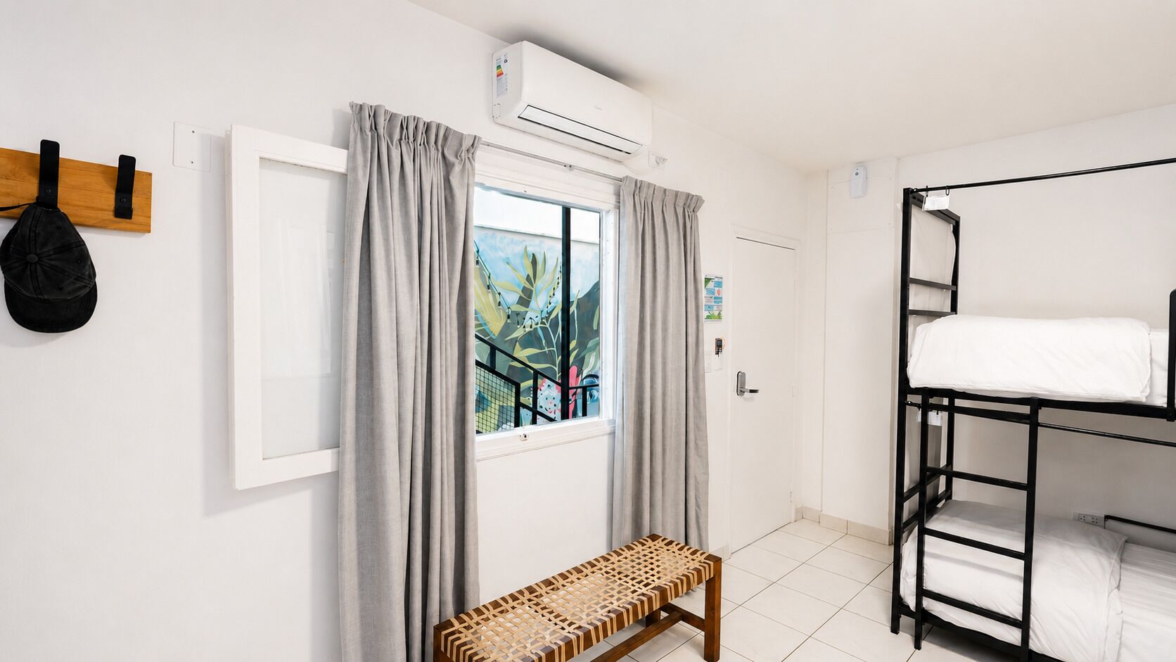 A room with a bunk bed, a bench, a window with curtains, and an air conditioning unit.