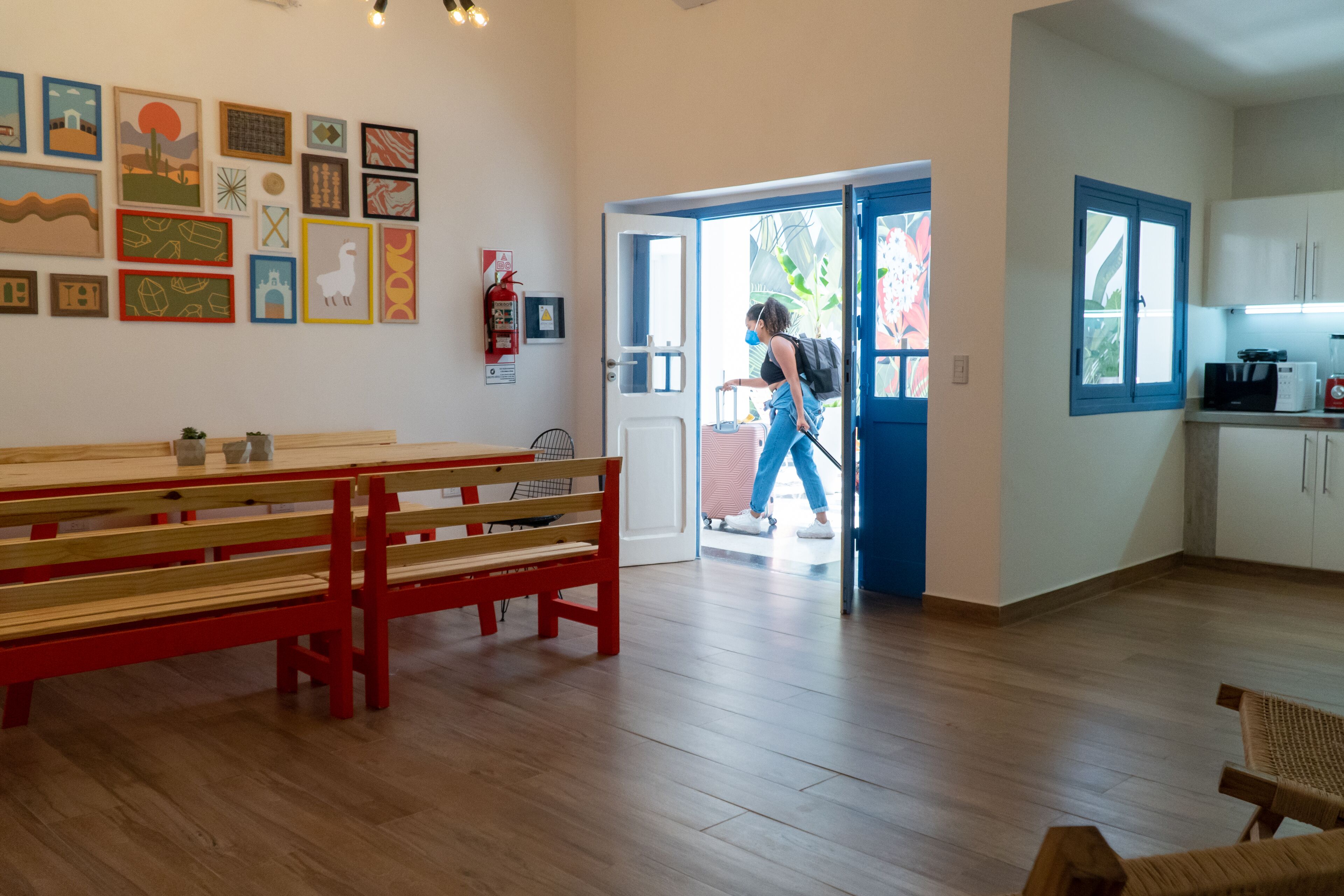 Una habitación con un banco de madera, una puerta que da al exterior y una zona de cocina con armarios y un microondas.