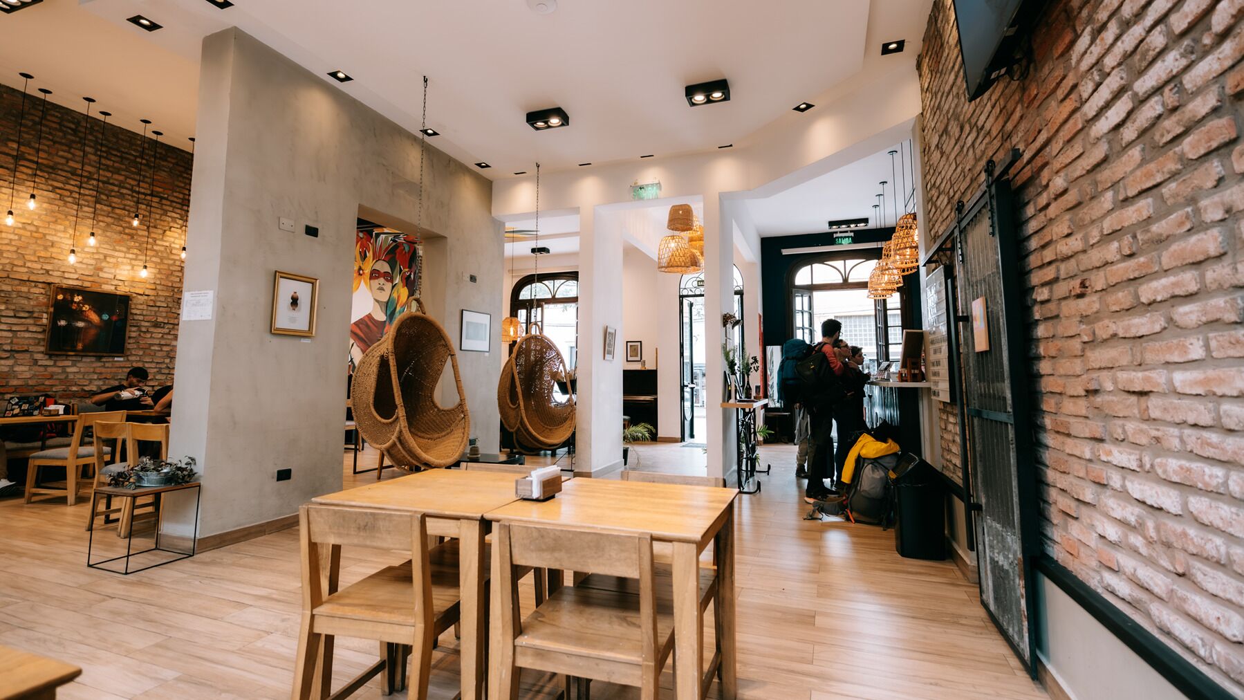 Interior de restaurante com mesas de madeira, cadeiras penduradas e paredes de tijolo.