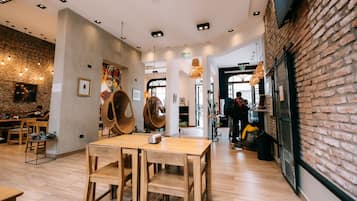 Interior de restaurante com mesas de madeira, cadeiras penduradas e paredes de tijolo.