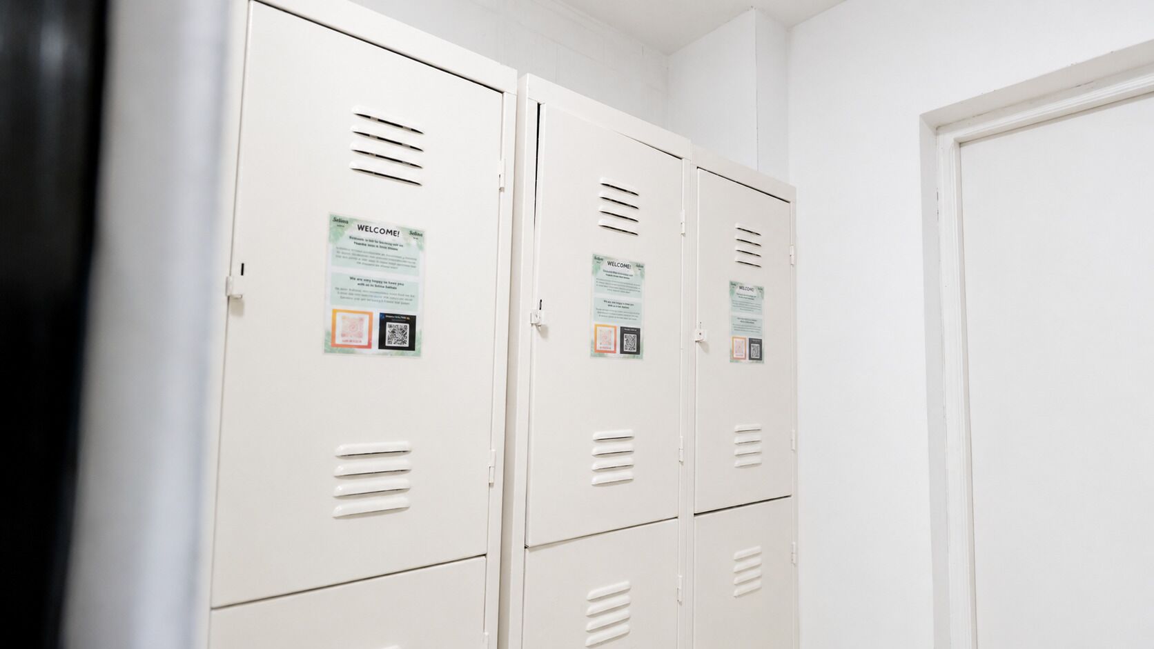 A row of white lockers with QR codes and welcome signs.