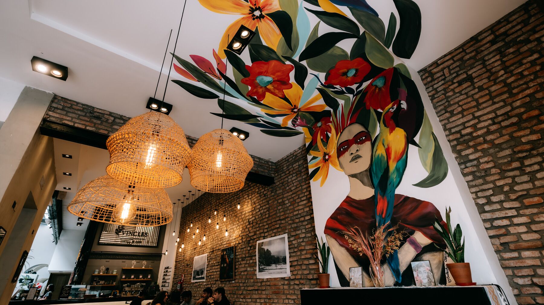 A restaurant interior with exposed brick walls, pendant lighting, and a mural of a woman with a bird.