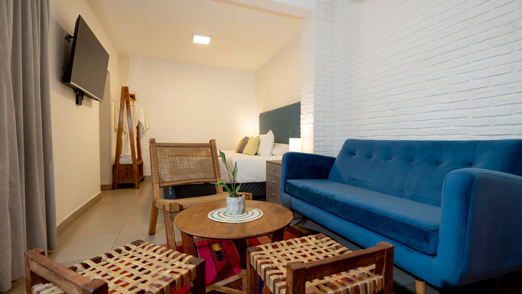 Ein modernes Wohnzimmer mit einem blauen Sofa, Korbstühlen, einem kleinen runden Tisch mit einer Pflanze und einem an der Wand befestigten Fernseher.