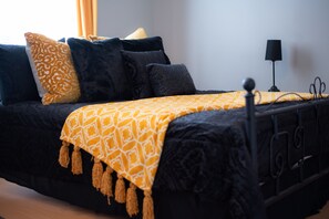 Un lit avec un cadre noir, une couverture jaune à motifs et plusieurs coussins noirs et jaunes.