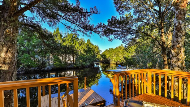 Une terrasse en bois avec un bateau amarré sur la droite, entourée d’arbres et bordée d’une étendue d’eau calme.
