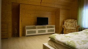 A wooden-paneled room with a bed, a television on a cabinet, a chair, and a window with curtains.
