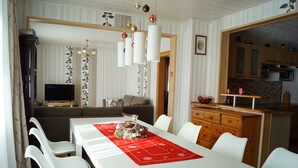 A modern living room with a white sofa, a dining table with a red placemat, and a kitchen area with wooden cabinets.