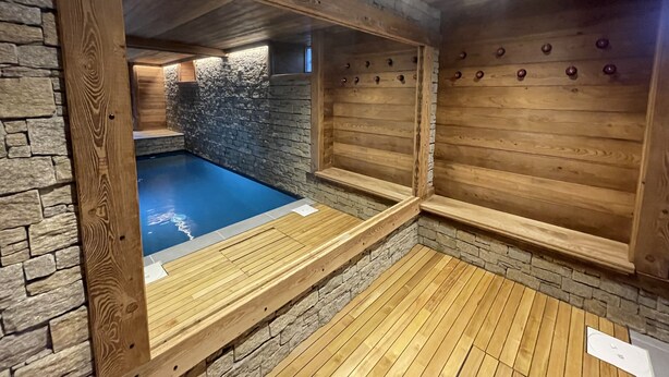 Een wellnessruimte met een stenen muur, houten banken en een zwembad in blauwe tinten.
