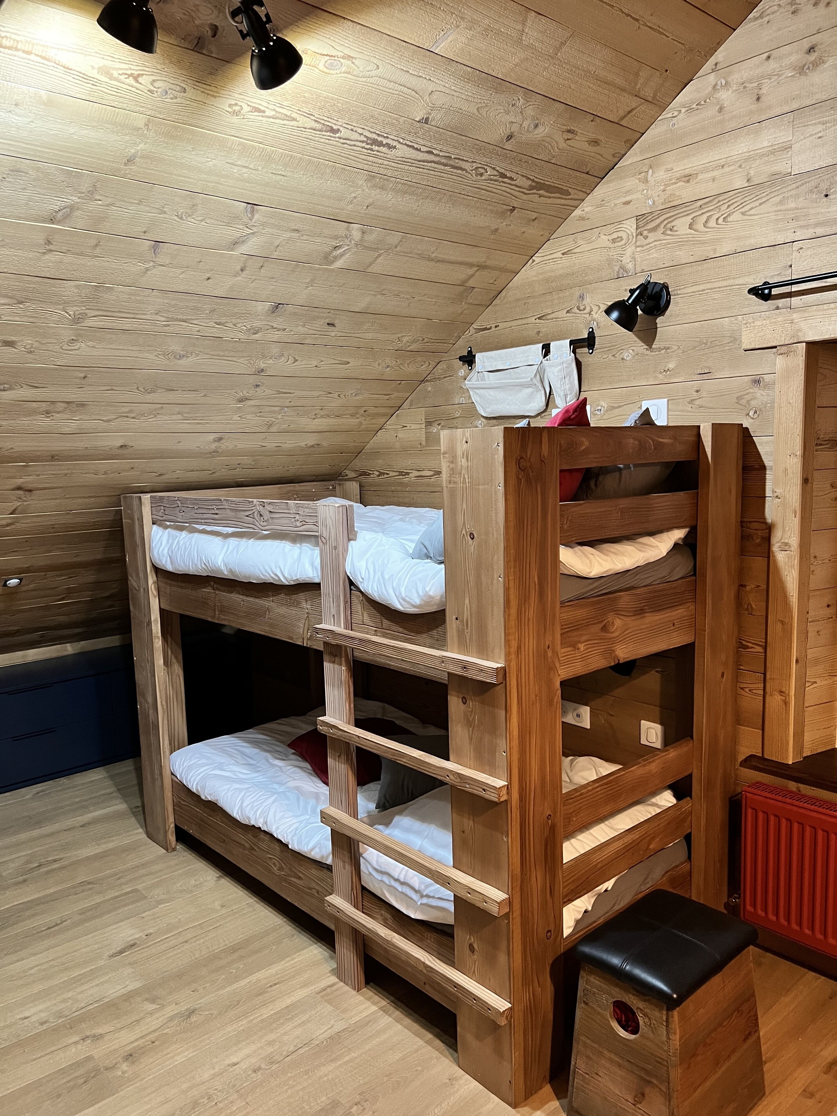 En køjeseng i træ med en stige, en rød radiator og en lille skammel.