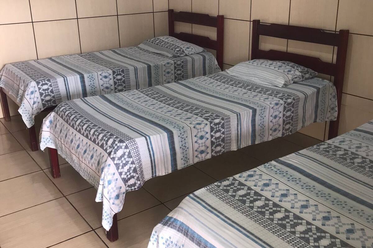 A room with two single beds, each with a patterned bedspread and wooden headboards. The room has tiled walls and floors.