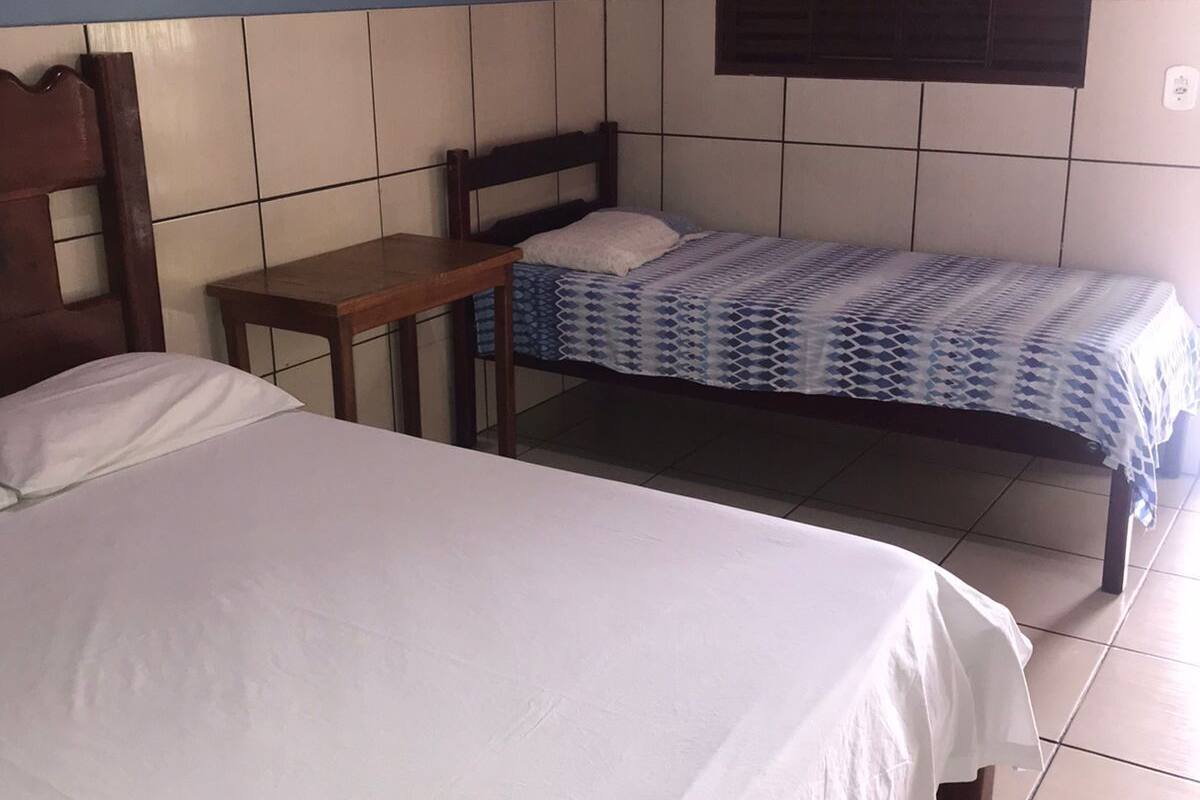 A room with two beds, one larger and one smaller, a wooden table, and a window with blinds.