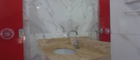 A bathroom with a marble sink and two faucets, a red door, and a mirror.