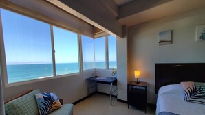 Una habitación de hotel con cama, escritorio, silla y vista al océano.