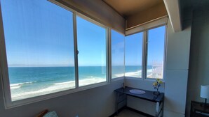 Habitación con amplia ventana con vista al océano, una kitchenette pequeña y un sofá con un cojín estampado.