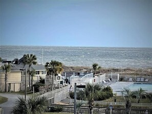 A beachfront property with a swimming pool, palm trees, and a view of the ocean.
