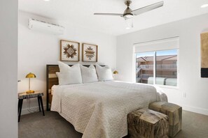 Een slaapkamer met een bed, een plafondventilator, een airconditioningapparaat, een raam met uitzicht en twee kunstwerken aan de muur.