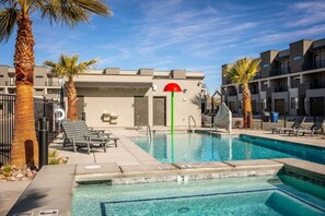 Una piscina con sillas de descanso y palmeras, rodeada de edificios modernos.