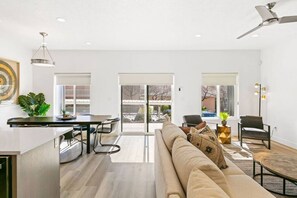 Een moderne woonkamer met een bank, een eethoek met een tafel en stoelen, en een keuken met een aanrecht.