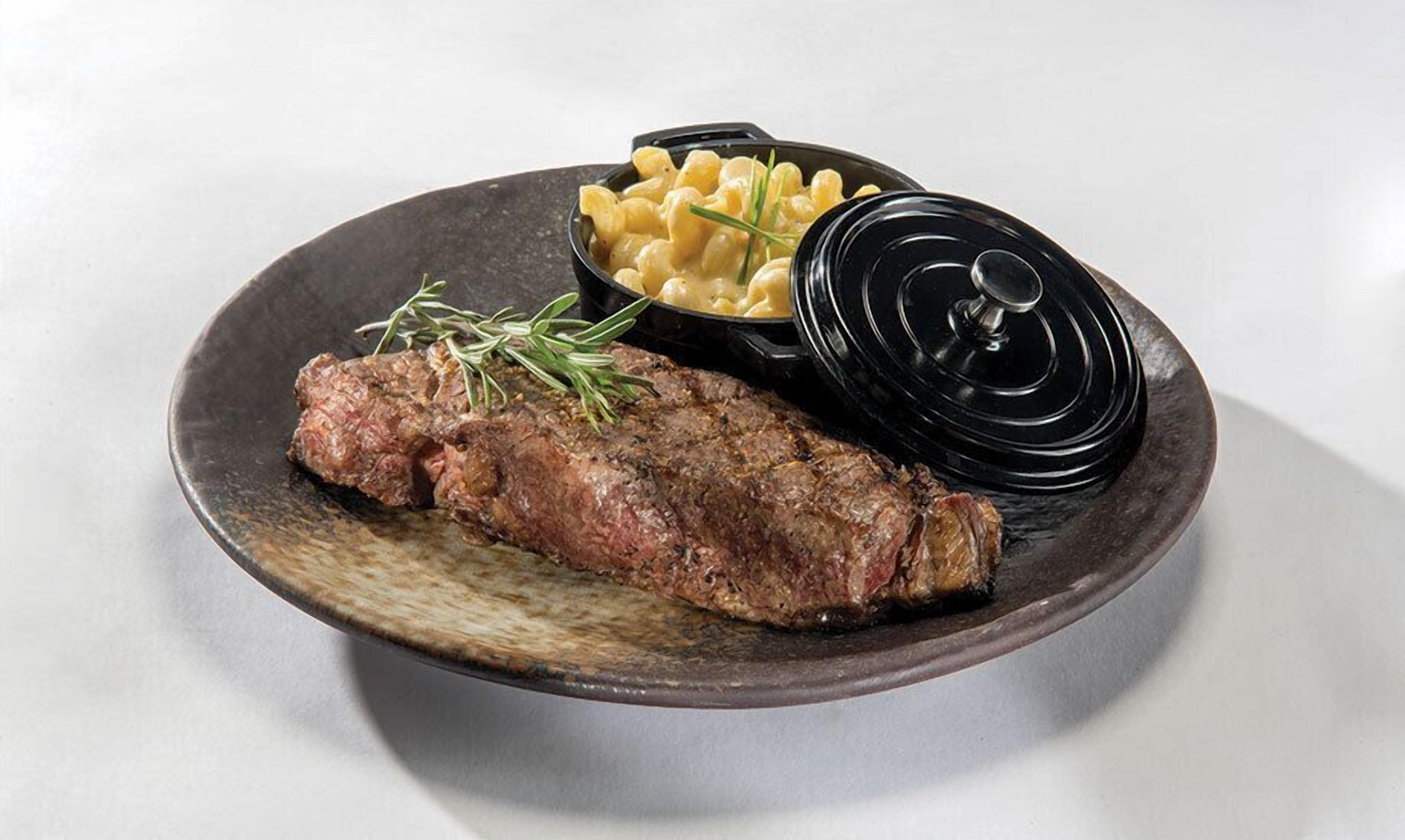 A plate with a steak, macaroni, and a black lid.