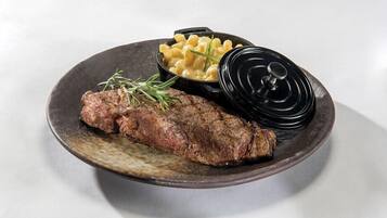 A plate with a steak, macaroni, and a black lid.