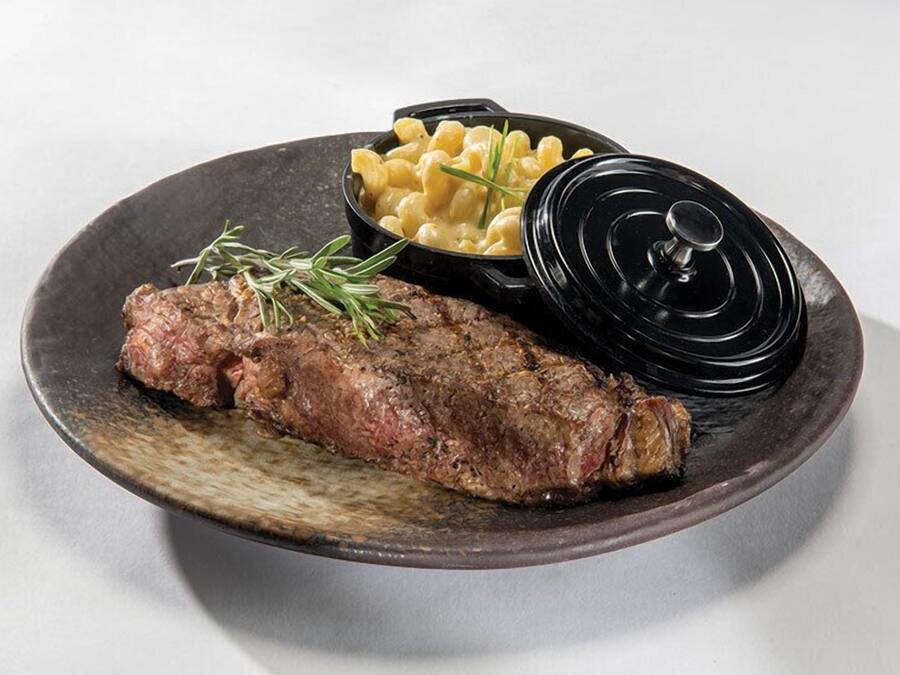 A plate with a steak, macaroni, and a black lid.