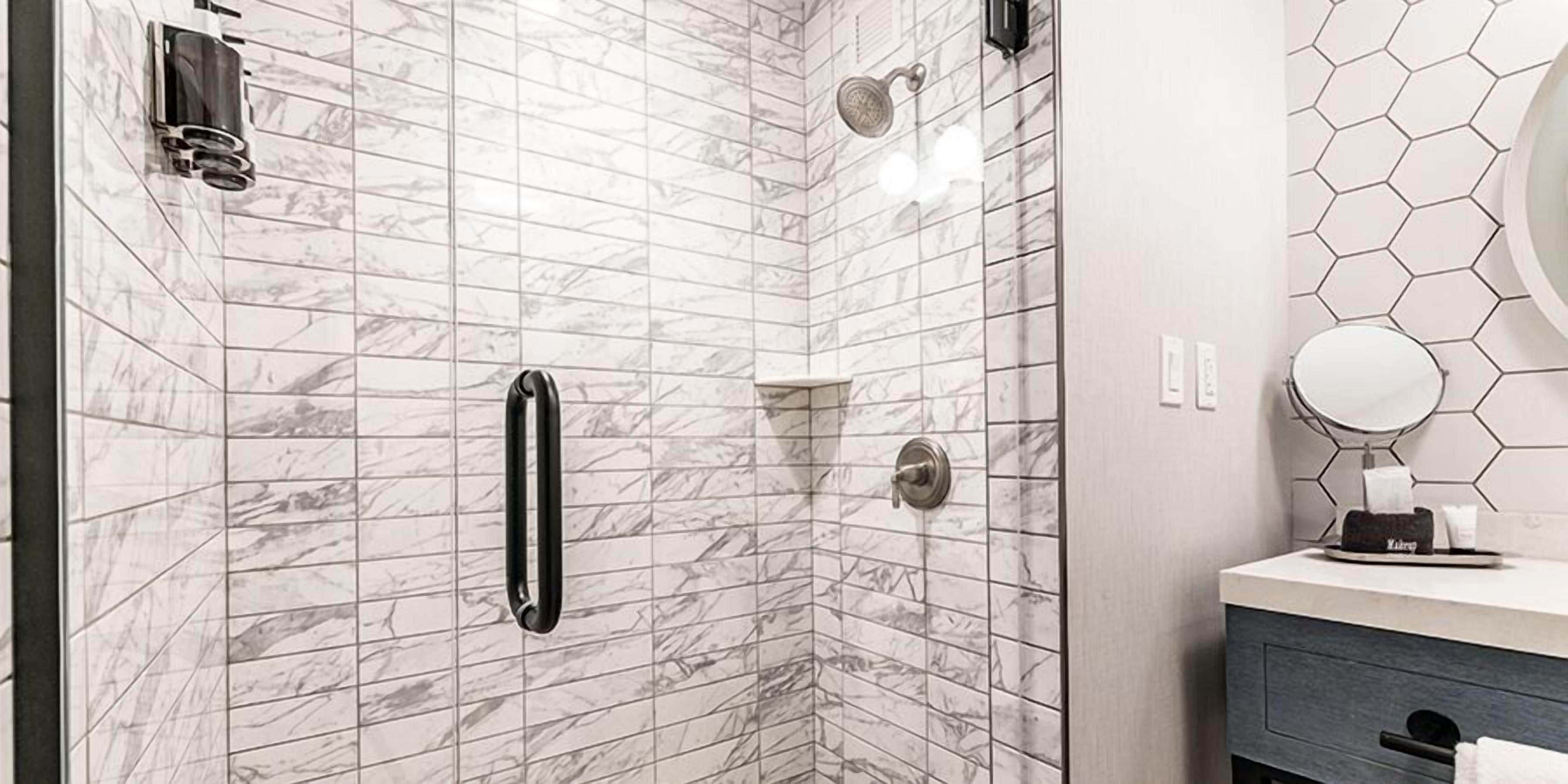 Une salle de bain moderne avec une douche d’angle, une barre d’appui, des toilettes et un meuble-lavabo avec un miroir.