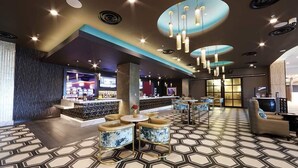Un hall d’hôtel moderne avec un bar, des espaces aménagés pour s’asseoir et un sol à motifs.