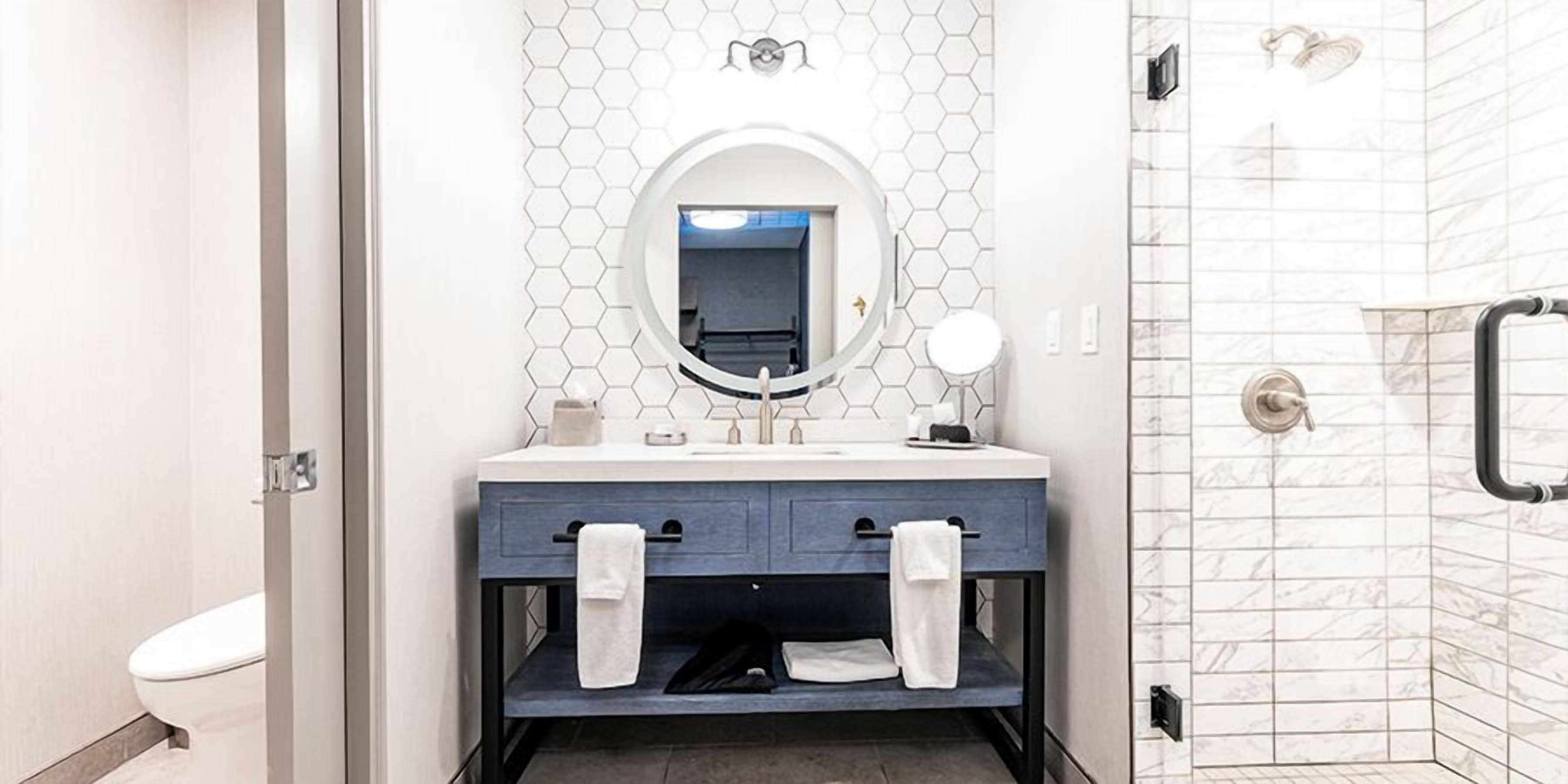 A modern bathroom with a white toilet, a blue vanity with a mirror, and a shower area.