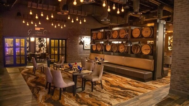 L’intérieur d’un restaurant avec un bar, des tables et un mur décoré de barils en bois.