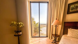 A hotel room with a bed, a potted plant, a lamp, and a view of the beach through a large window. - Where the Beach meets luxury! BEACHFRONT! (Pensacola)