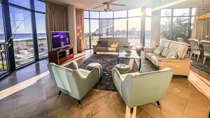 A spacious living room with a large TV, comfortable seating, and a view of the ocean. - Where the Beach meets luxury! BEACHFRONT! (Pensacola)