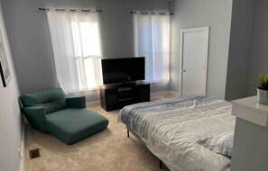 A bedroom with a bed, a TV, a green sofa, and a door.