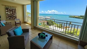 A balcony with wicker furniture, a glass table, and a view of a marina and ocean.