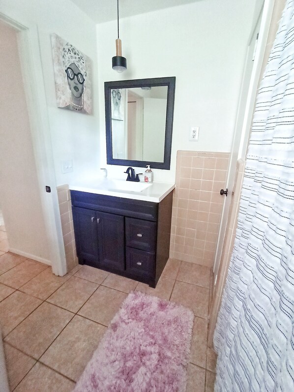 A bathroom with a white sink, dark cabinets, a mirror, and a pink rug.
