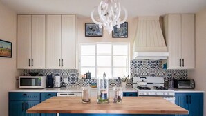 A kitchen with a wooden island, blue cabinets, a microwave, a stove, and a chandelier.