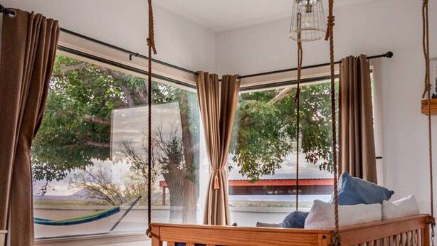 A room with a hanging bed, large windows, and a view of the outdoors.